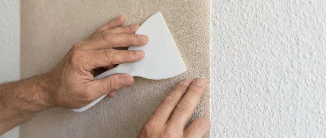 Detalle de papel pintado grueso colocándose sobre una pared con gotelé